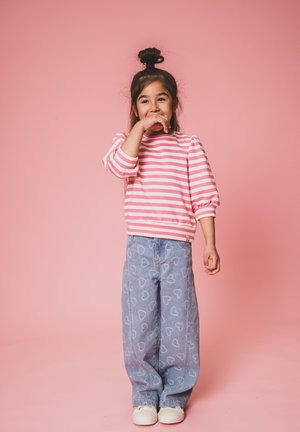 Gestreepte roze en witte sweater met pofmouwen, gecombineerd met lichtblauwe jeans met hartpatronen. Witte sneakers maken de outfit compleet.