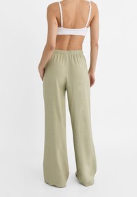 Lichtgroene linnen broek met brede pijpen en een elastische tailleband, met een gladde textuur en een losse pasvorm. Achteraanzicht weergegeven.
