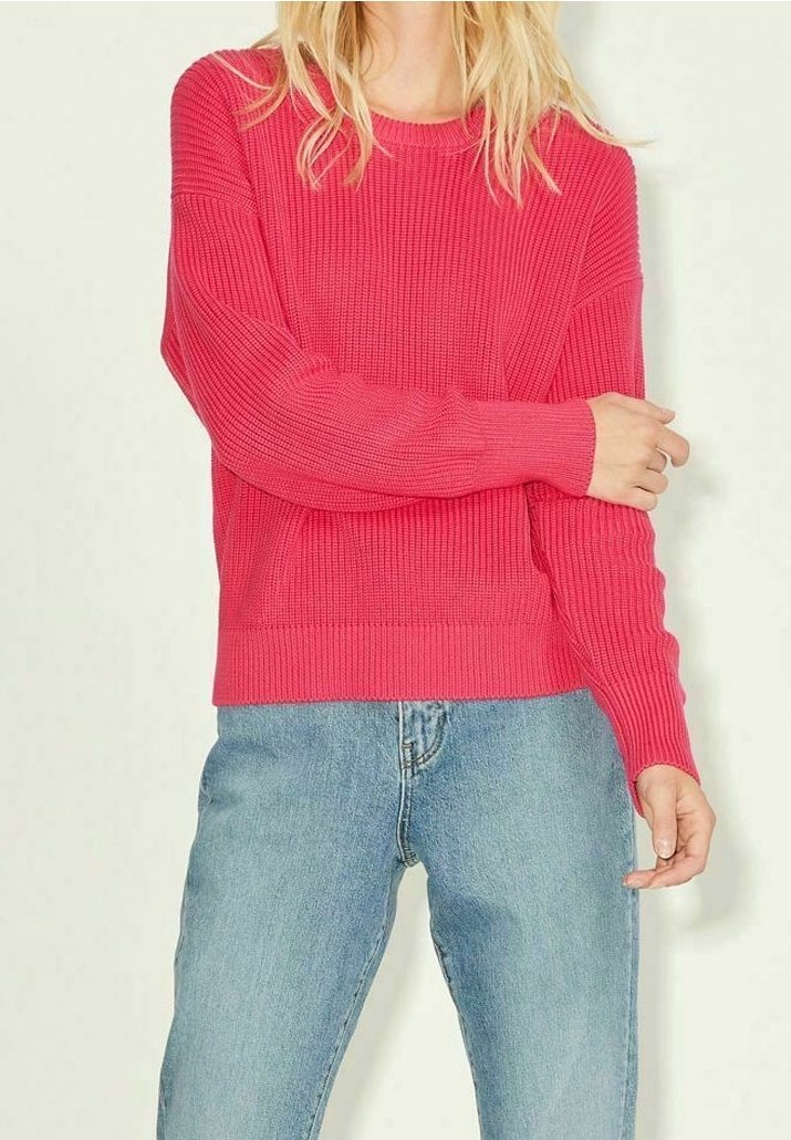 Maglione rigato di un vivace colore rosa con maniche lunghe e collo rotondo, abbinato a jeans azzurri chiari. Il maglione ha una vestibilità ampia e un design testurizzato.
