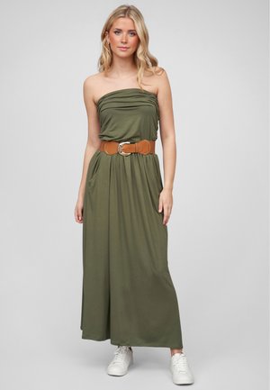 Olijfgroene maxi-jurk met een strapless ontwerp, textuur draping, zijzakken en een bruine riem. Gecombineerd met witte sneakers.