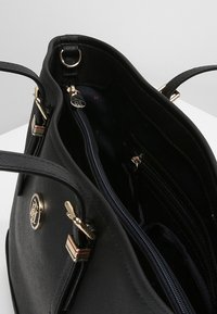 Černá kožená kabelka s dvojitými ušima, zlatým kováním a zipovým vnitřním oddílem s dalšími kapsami uvnitř.