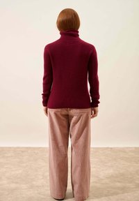 Bordowy sweter z golfem o prążkowanej fakturze, zestawiony z jasnoróżowymi spodniami dzwonami z sztruksu, widok z tyłu.