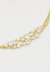 Collar de cadena de oro con múltiples piedras preciosas claras en varias formas, incluyendo rondas y cuadradas, con tamaños y engastes alternos.