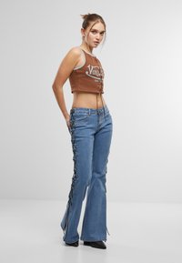 Brun cropped tank topp med snøring foran, kombinert med lyseblå utsvingte jeans med svarte blonder på sidene.