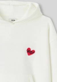 Sweat à capuche blanc en tissu doux, comportant une broderie rouge en forme de cœur avec le texte « Joueur Certifié ». Capuche et poche avant incluses.