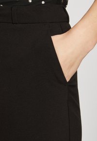 Zwarte broek met een gladde stoftextuur, voorzien van een zijzak en een aangesloten taille. Het ontwerp is op maat gemaakt voor een slanke silhouette.