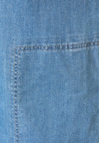Tessuto denim blu chiaro, con una tasca a pattina con cuciture visibili. La texture appare morbida con una finitura leggermente sbiadita.