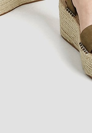 Wedge espadrille med en vævet jute platform og en blød olivengrøn stofoverdel. Har sølvfarvede hardware detaljer på siderne.