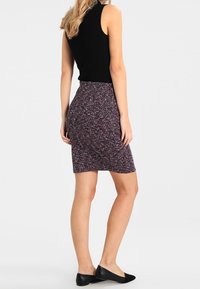 Haut noir sans manches assorti à une jupe crayon longueur genou avec un motif zigzag en rouge, blanc et bleu marine, complété par des ballerines noires.