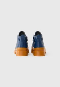 Par de botas de tornozelo de couro azul com solas de borracha grossas e castanhas, mostradas de costas contra um fundo branco.