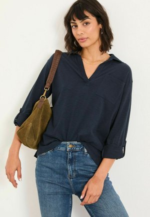 Navy blue long-sleeve shirt with a collared neck and chest pocket, paired with light blue denim jeans and a brown shoulder bag.