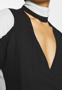 Schwarzes tiefes V-Kleid mit grauen Akzenten, das einen eleganten Kragen aufweist. Der Stoff wirkt glatt und betont den klaren Schnitt und das Design.