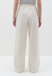 Pantalones de pierna ancha en color crema con cintura elástica y textura suave, que presentan un diseño minimalista y sin adornos visibles.