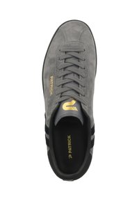 Zapatilla de ante gris con rayas negras, puntera redonda y suela plana. Presenta un logo dorado en el costado y la lengüeta con un diseño de cordones. El interior es negro.