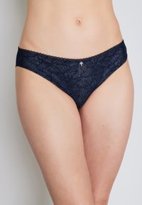Marineblaue Spitzen-Bikini-Höschen mit floralem Muster, gewellten Rändern und einem kleinen metallischen Akzent an der Vorderseite. Weiche, durchsichtige Textur.