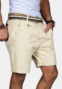 Beige shorts with rolled hems, featuring side pockets and a front button closure. Paired with a multicolored woven belt.