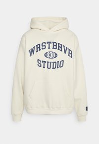 Krémová mikina s kapucí vyrobená z měkkého materiálu má přední kapsu, žebrované manžety a výrazné tmavě modré grafické logo na hrudi.