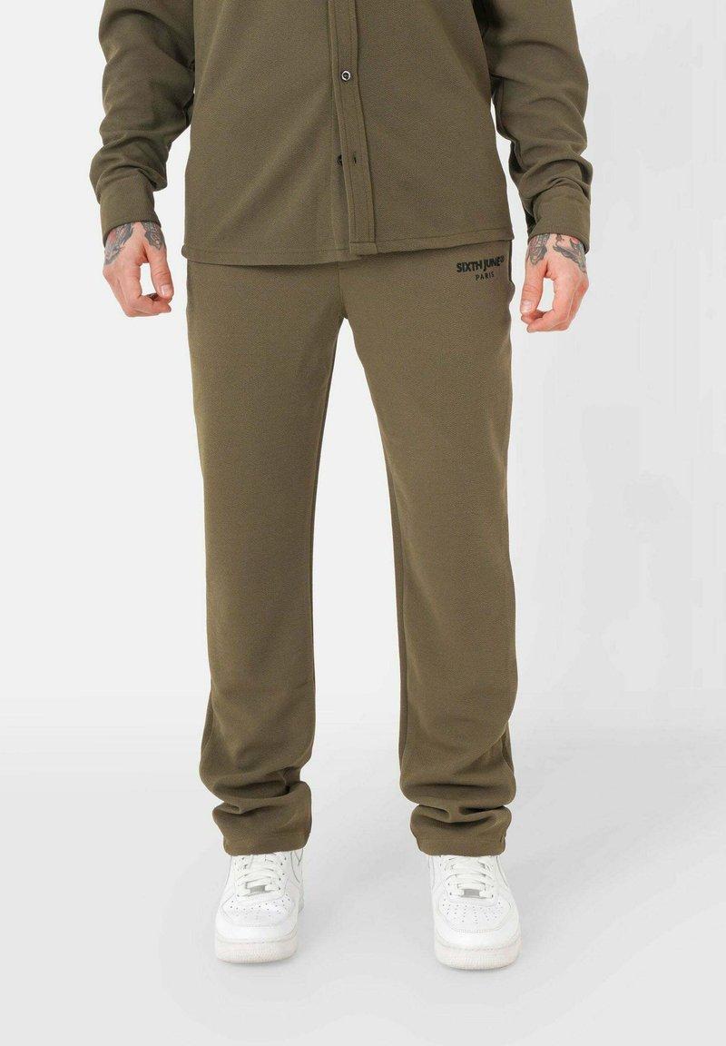 Olijfgroene sweatpants gemaakt van zacht materiaal, met een relaxed fit en een elastische tailleband, gecombineerd met witte sneakers.