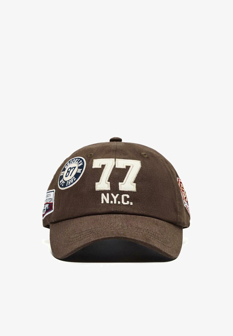 Casquette de baseball marron avec « 77 N.Y.C. » brodé sur le devant et patch rond « Brooklyn 87 » sur le côté.