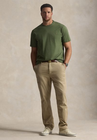 Χακί βαμβακερό μπλουζάκι με στρογγυλή λαιμόκοψη; χακί βαμβακερό παντελόνι με τσέπες; κρεμ αθλητικά παπούτσια; διακριτικό λογότυπο στο μπλουζάκι.