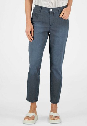 Frau trägt kurze marineblaue Nadelstreifenhosen mit fünf Taschen und weiße Plateausandalen, steht mit einer Hand in der Tasche.