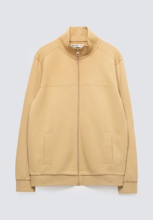Béžová bunda na zip s límečkem do stojáčku, dlouhými rukávy, dvěma předními kapsami a žebrovanými manžetami a lemem.