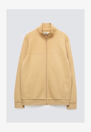 Beež toonides lukuga jakk kõrge kaelusega, pikkade varrukate, kahe eesmise tasku ning soonikkoes varrukate ja äärega.