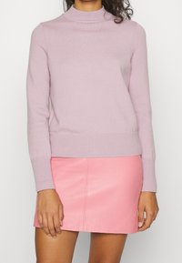 Pull en maille violet clair avec un col montant et des poignets côtelés, associé à une jupe en cuir rose ajustée avec une couture frontale.