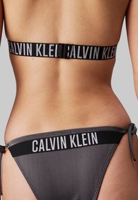 Ensemble de bikini à rayures noires et blanches, présentant une bande élastique avec logo à l'arrière. Le haut dispose d'une fermeture à clip, et le bas a des lanières à nouer sur les côtés.