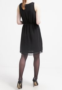 Robe noire sans manches avec une taille cintrée, longueur genou, fabriquée en tissu léger, associée à des escarpins noirs.