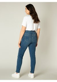 Skinny jeans van donkerblauwe denim, hoge taille, met achterzakken en subtiele stikdetails. Gecombineerd met een wit T-shirt en sneakers.