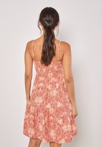 Robe d'été à motif rouge et orange avec de fines bretelles, un buste smocké et une jupe à volants. Tissu léger avec un design floral et géométrique.