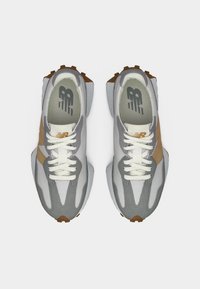 Een paar atletische sneakers in grijs en bruin met witte veters, gezien van bovenaf op een witte achtergrond.