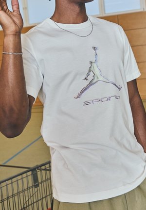 Bílá bavlněná tričko s reflexním logem Jumpman a slovem "SPORT" v stříbrné barvě pod ním. Kulatý výstřih, krátké rukávy, volný střih.