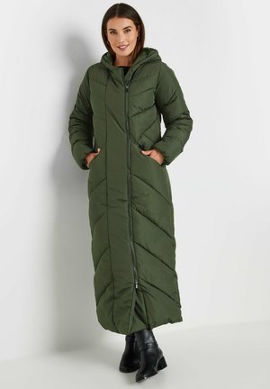 Lang groen pufferjack met capuchon, voorzien van een rits aan de voorkant, schuin quilt patroon en zijzakken. Draagt met zwarte enkellaarsjes.