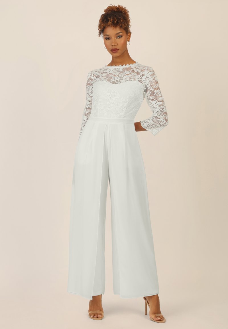 Weißer Jumpsuit mit einem Spitzen-Longsleeve-Oberteil, geraden, weiten Beinen und einer gefalteten Taille. Glattes Material mit einer taillierten Silhouette.