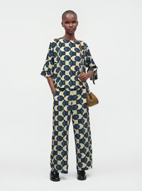 Personne portant un haut et un pantalon large à motifs géométriques assortis, tenant un petit sac à main marron tressé avec une bandoulière chaîne.