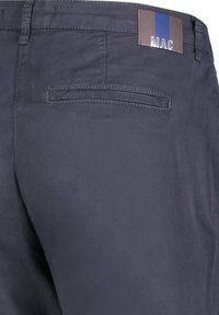 Dunkelblaue Hose mit glatter Textur, ausgestattet mit einer Gesäßtasche und einem braunen Etikett mit blauen und braunen Streifen in der Nähe des Taillenbunds.