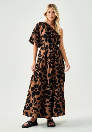 Maxi dress in brown fabric with black floral pattern, one-shoulder design, tiered skirt, and cinched waist. Paired with black sandals.