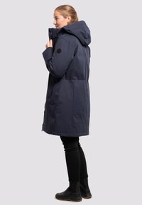 Abrigo largo de color navy con capucha, cierre con cremallera en el frente y bolsillos laterales. Presenta una tela suave e impermeable y un parche de logo en la manga izquierda.