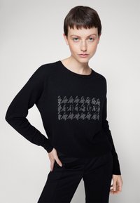 Maglione nero realizzato in morbido tessuto, con un motivo houndstooth testurizzato in grigio sulla parte anteriore. Maniche lunghe e scollo rotondo.