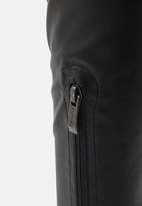 Bota de cuero negro con textura suave, que presenta una cremallera lateral de metal plateado. La cremallera recorre el exterior de la bota.