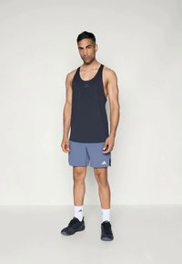 Débardeur de sport sans manches, bleu marine, avec un logo réfléchissant, associé à un short bleu clair, des baskets noires et des chaussettes blanches.