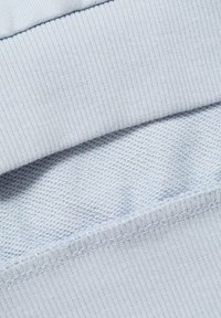 Material de culoare albastru deschis, care prezintă o textură canelată în partea de sus și o textură netedă, țesută în partea de jos, cu cusături vizibile de-a lungul marginilor.