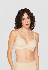 Beige bra with a smooth, seamless design, v-neck shape, and adjustable straps. Fabric appears stretchy and soft, ideal for comfort.