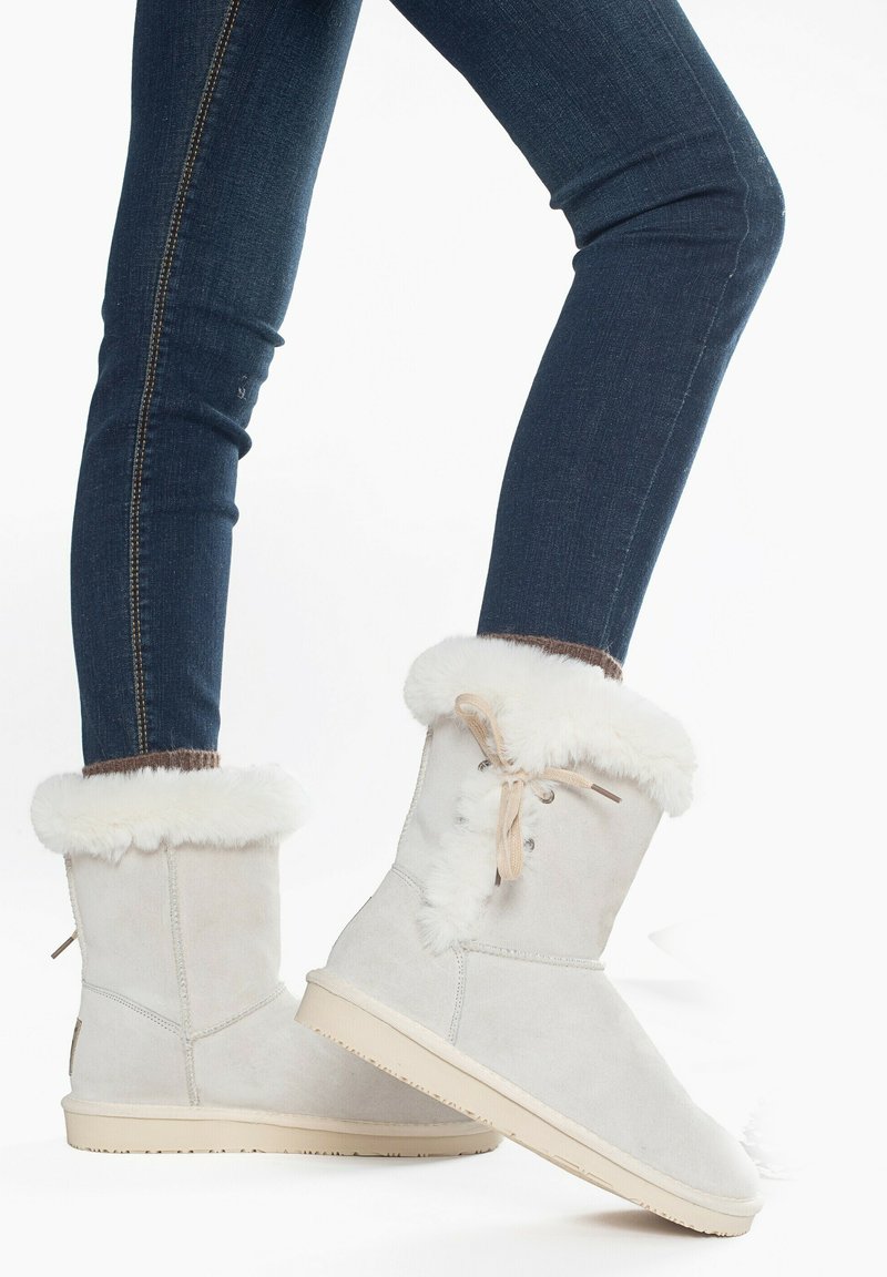 Ljusgrå mocka ankboots med vita syntetiska pälskanter, med en snöraccent och en beige gummisula. Passar bra ihop med mörka denimjeans.
