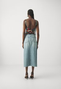Vista posteriore di una modella che indossa un crop top colorato e con fantasia, con sottili spalline, e una gonna di jeans alta di colore blu chiaro.