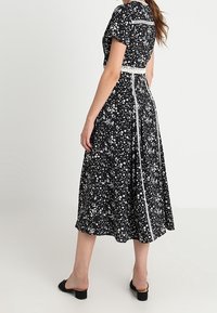 Svart blommig klänning med vita accenter, korta ärmar och ett knytbälte i midjan. Klänningen har en böljande knälång kjol med ett subtilt mönster.