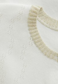 Vit stickad tyg med subtila blommönster och en gyllene ribbad halsringning, som visar en mjuk textur och delikata detaljer.