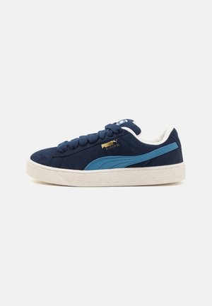 Granatowe buty sportowe Puma Suede z jasnoniebieskim paskiem, białą podeszwą i granatowymi sznurówkami, pokazane z profilu na białym tle.
